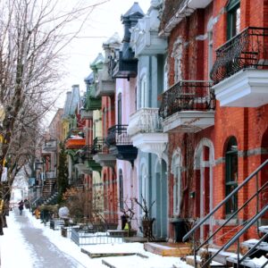 A sidewalk with two-story houses facing the sidewalk. The faces of the houses are in vibrant colours and with outdoor staircases and with balconies on the second floor facing the sidewal.